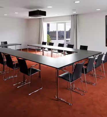 Ett modernt konferensrum med röd matta, med ett U-format arrangemang av svarta bord och stolar. Ett stort fönster med utsikt över staden är i bakgrunden, och ett abstrakt konstverk är monterat på den vita väggen.